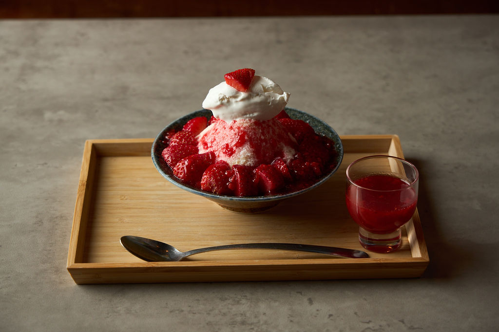 Strawberry milk kakigori on a bamboo tray with condensed milk and strawberry syrup